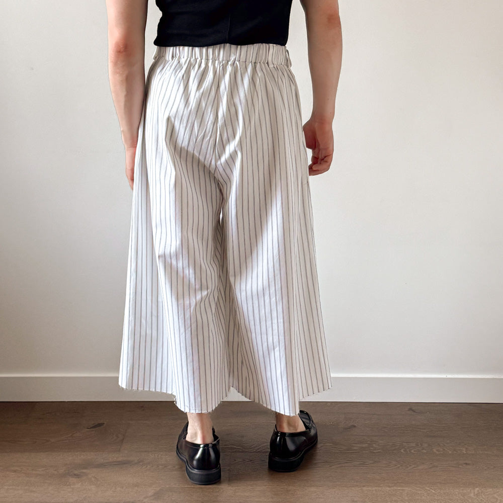 Person wearing white pants with thin black stripes and black shoes on a plain background