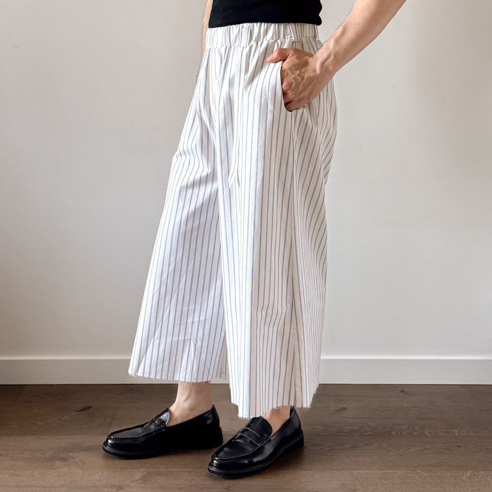 Person wearing white striped wide-leg pants and black loafers against a plain background