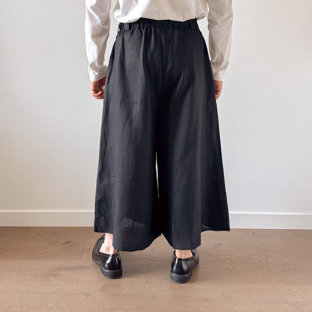 Person wearing black wide-leg pants and a light-colored shirt against a plain background