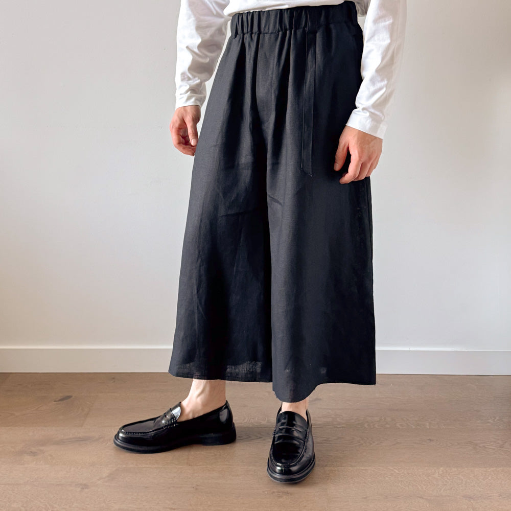 Person wearing black wide-leg pants and black shoes on a wooden floor.