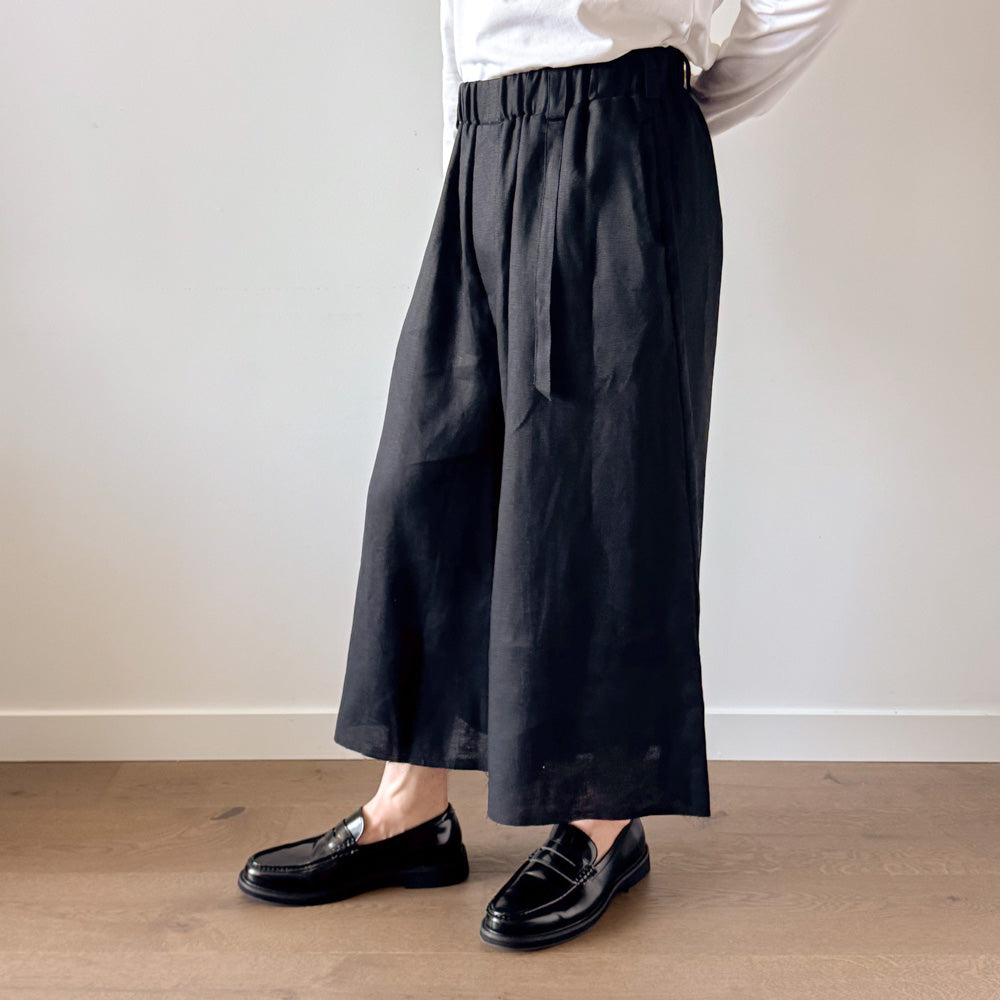 Person wearing black wide-leg pants and black shoes on a plain background