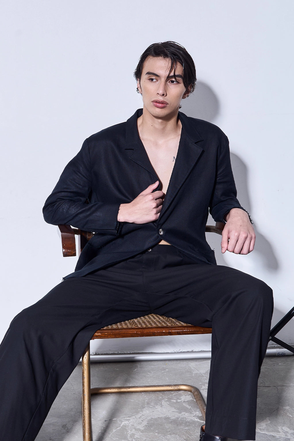 Man wearing a black outfit sitting on a chair against a white background