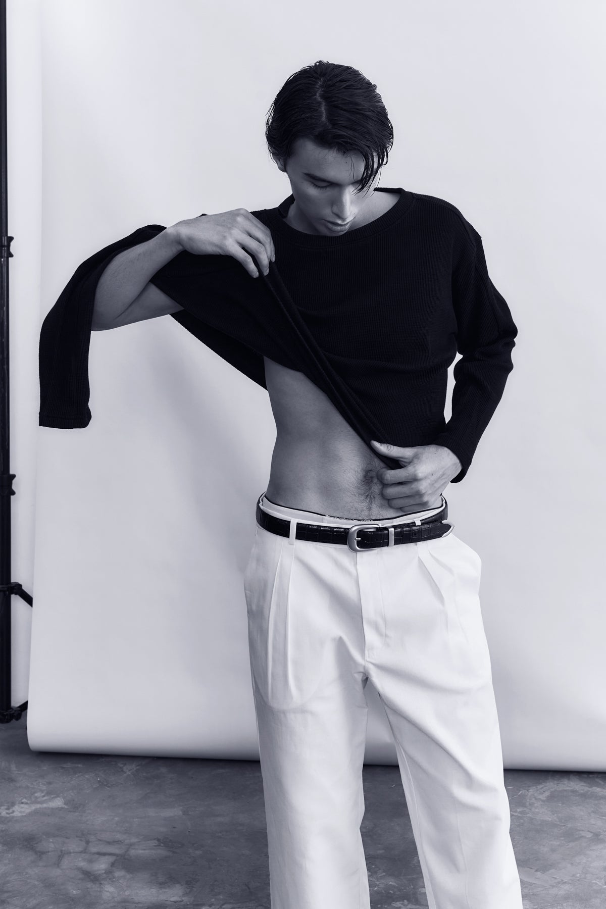 Man wearing a black sweater over white pants against a plain background