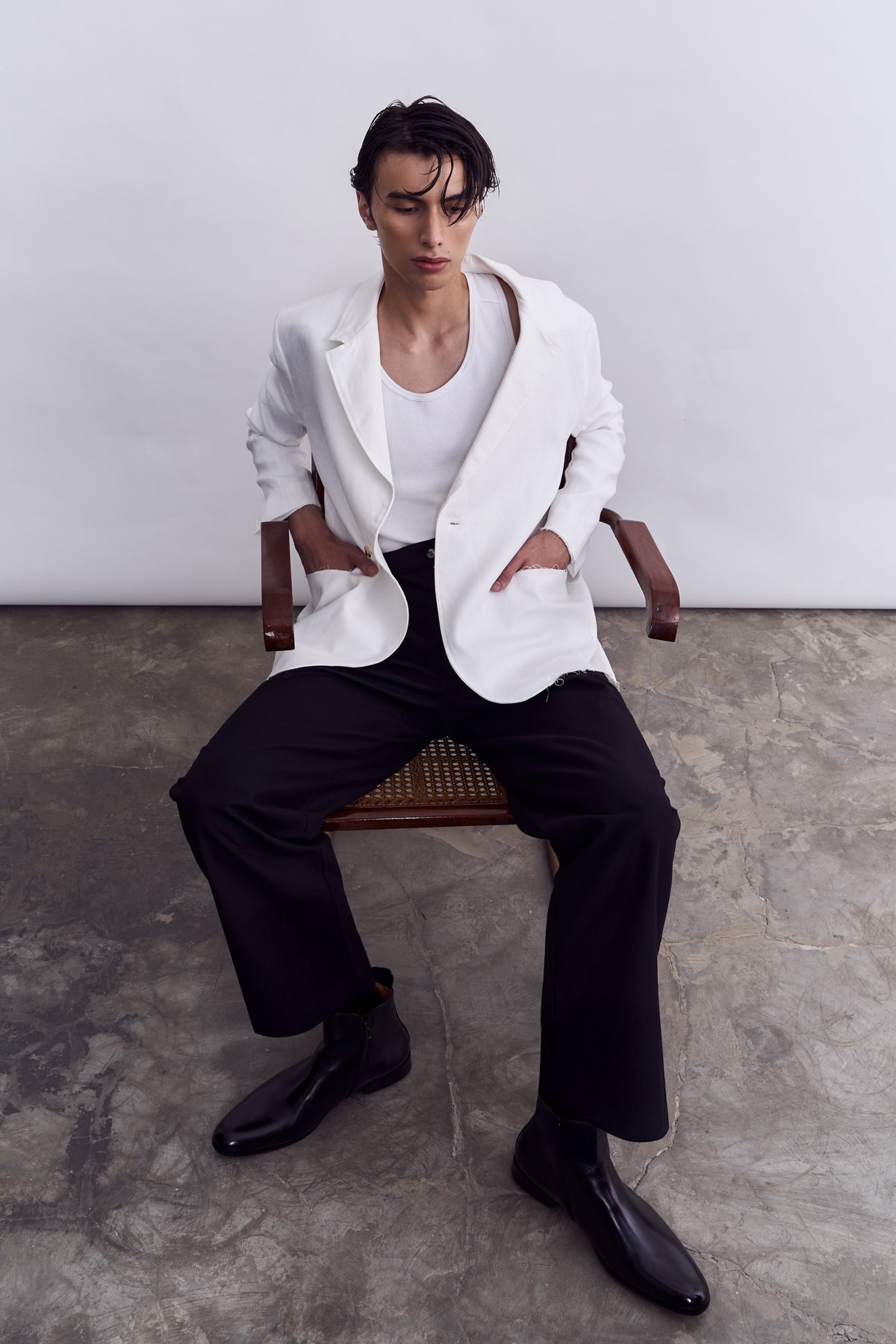 Man sitting on a chair wearing a white blazer, white shirt, and black pants.